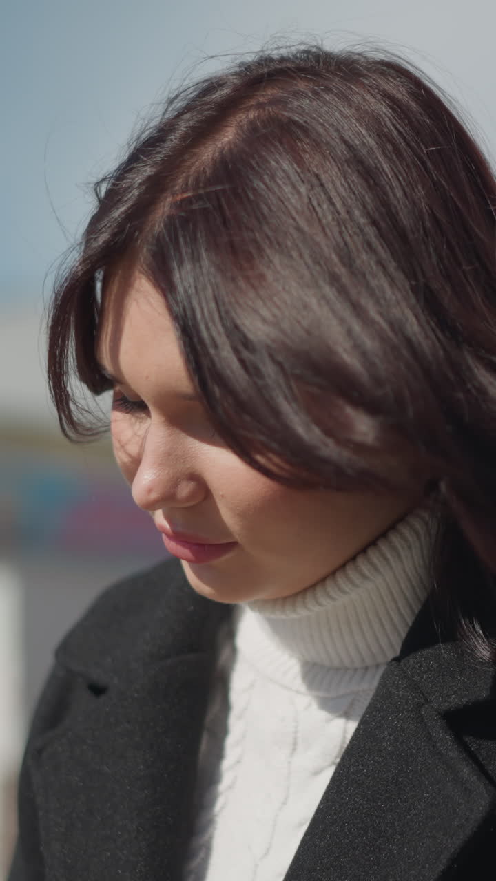 어떤 것에 초점을 맞추고 앉아있는 여성의 클로즈업, 빛에 비추고, 머리카락이 바람에 부드럽게 흔들리고, 부드러운 표정으로 멀리보고, 배경은 건축적 특징으로 흐릿합니다.