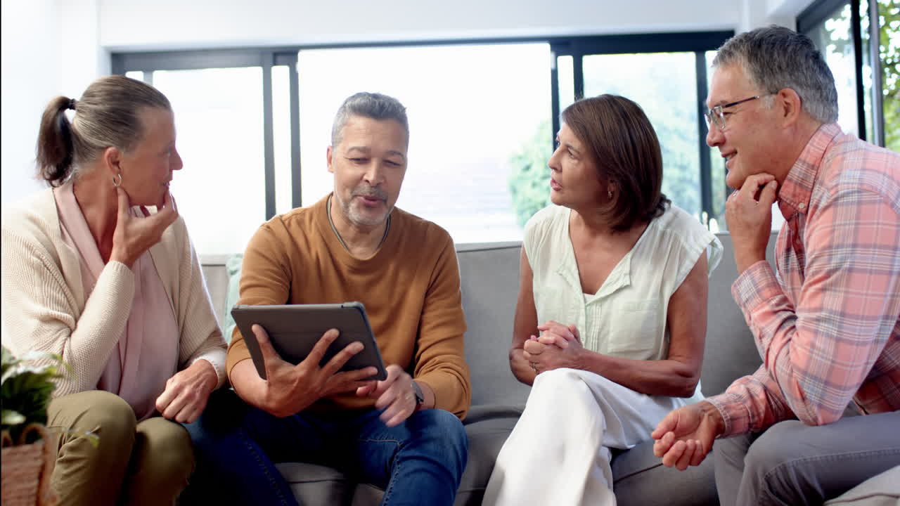 Group of senior friends sitting on couch, discussing something on tablet
