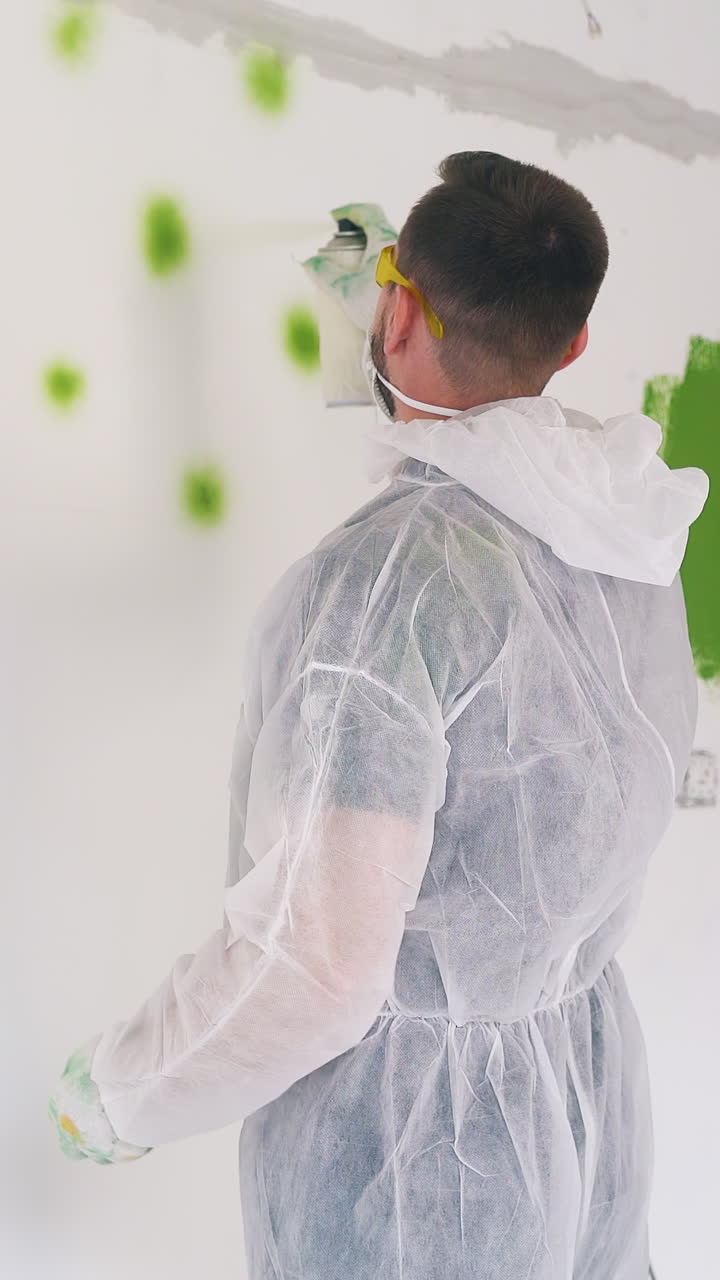 happy young guy and pretty girl in transparent coveralls and masks paint wall with sprays from bottles in renewing room