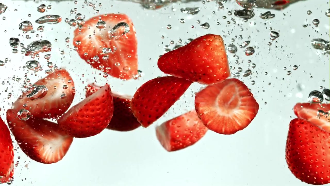 Fette di fragola fresche che cadono e schizzano in acqua limpida con bolle.