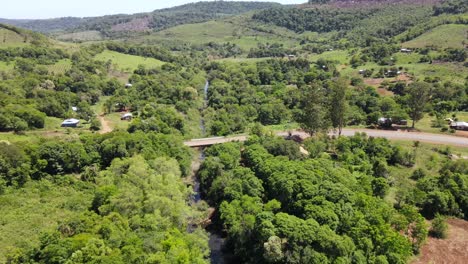 Una-Carretera-Panorámica-Atraviesa-El-Corazón-De-Un-Paisaje-Rural,-Cruza-Un-Pequeño-Río-A-Través-De-Un-Encantador-Puente,-Combinando-Naturaleza-Y-Transporte-En-Tranquila-Armonía