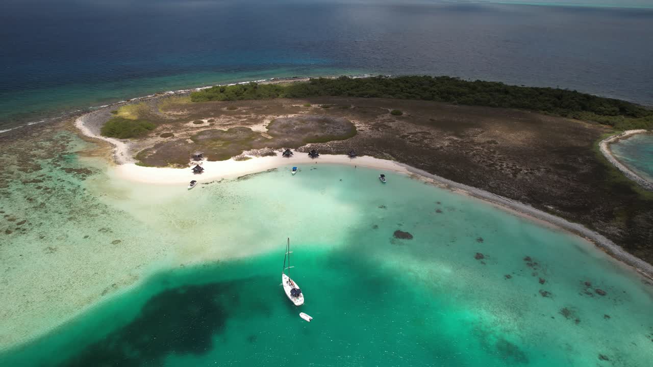 Boats anchored in turquoise waters near a remote tropical beach with lush landscape, aerial view