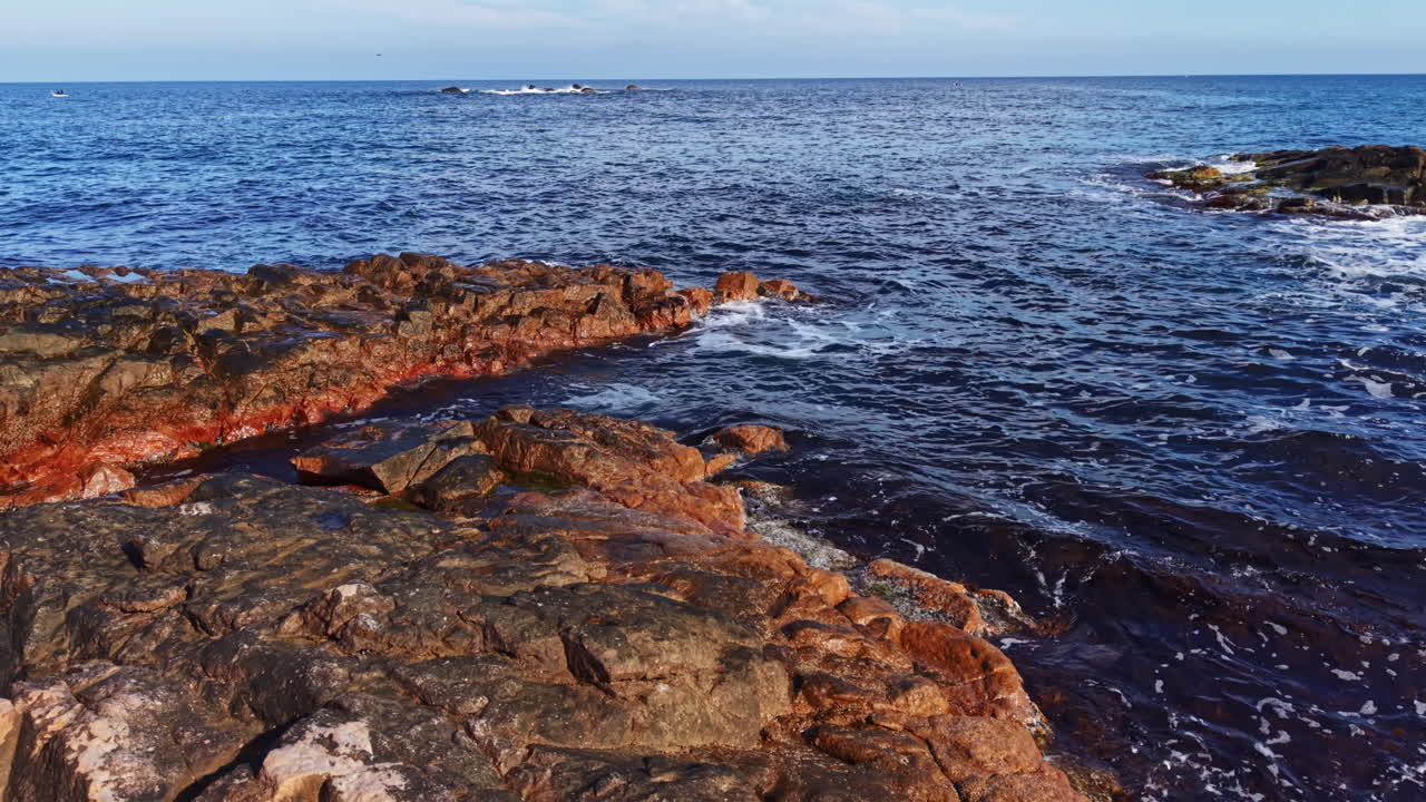 Litorale costiero vibrante al tramonto con formazioni rocciose e onde delicate che creano un'atmosfera marina serena.