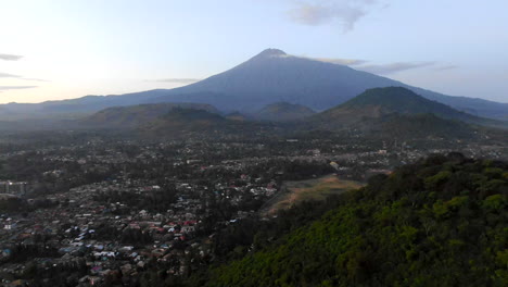 Drone-Shot-of-a-Huge-Mountain-Next-to-an-African-Village,-Backwards-Flying-Motion