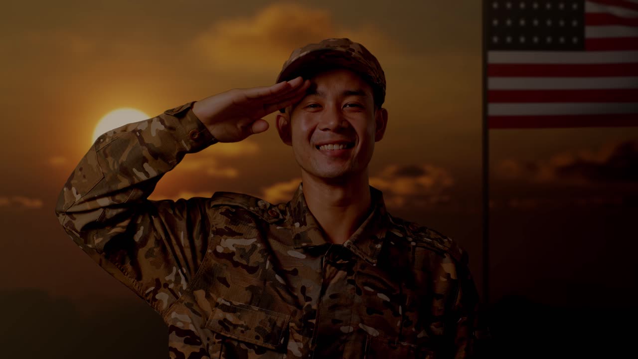 아시안 남성 군인이 미국 발을 들고 서서 인사를 하고 웃는 장면, 해가 지는 시간