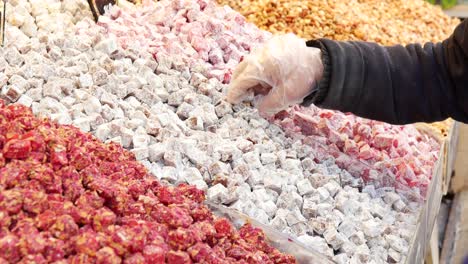 una mano se extiende para agarrar un puñado de delicias turcas de una exhibición de diferentes sabores y colores.