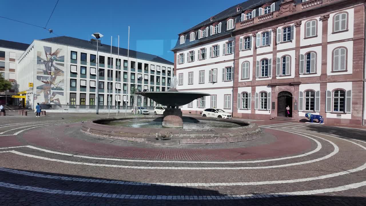 Shadow of the tram passing over city sqaure Brunnen Luisen with people waiting, a fountain and historical buildings. Germany, Darmstadt. View from the tram