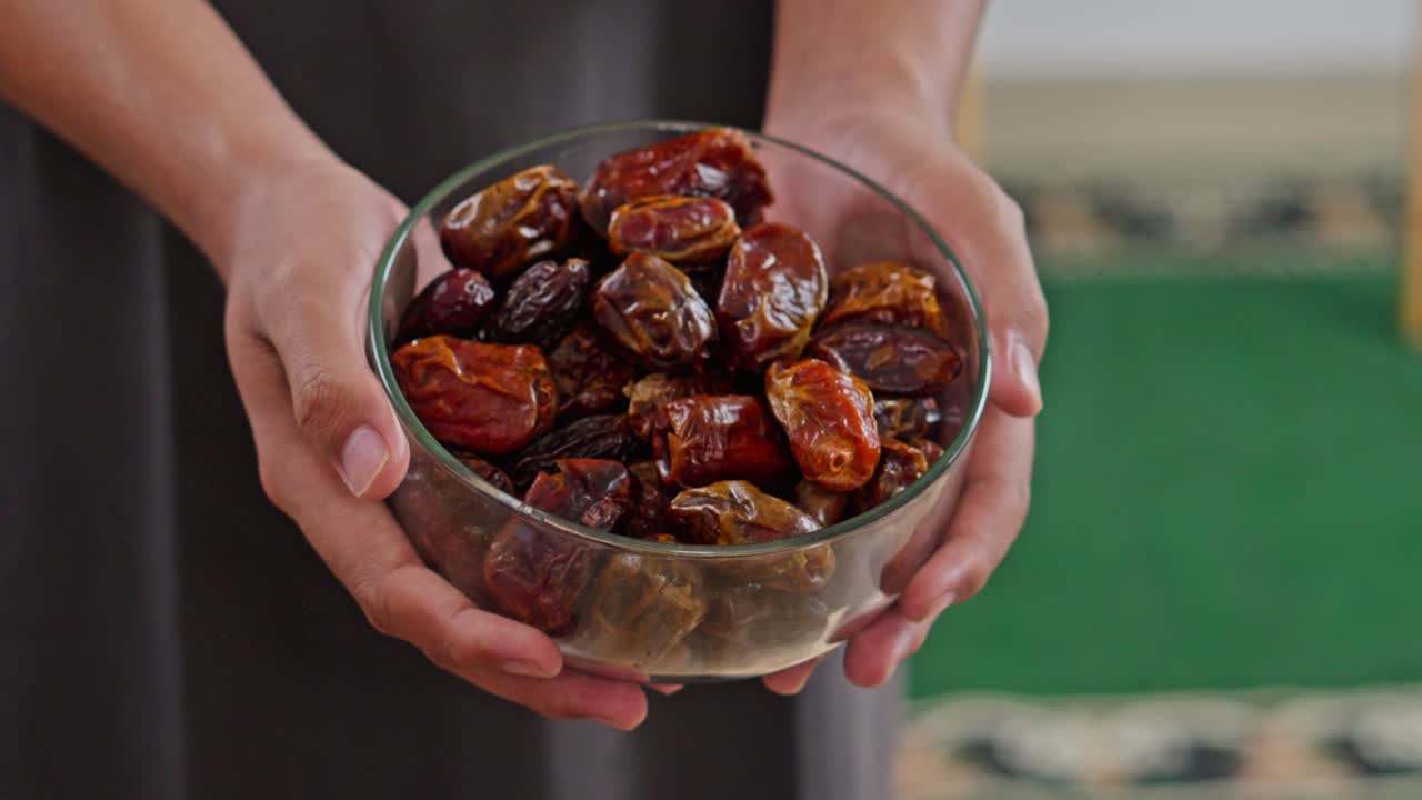 Close-up of Hands sharing dried dates from glass bowl during religious or cultural gathering