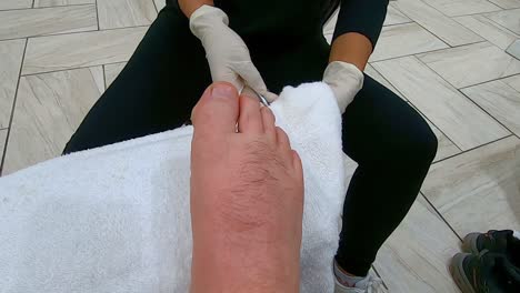 professional pedicurist with gloves trims the cuticles and extra skin from a man's right pinky toes by using a cuticle nippers