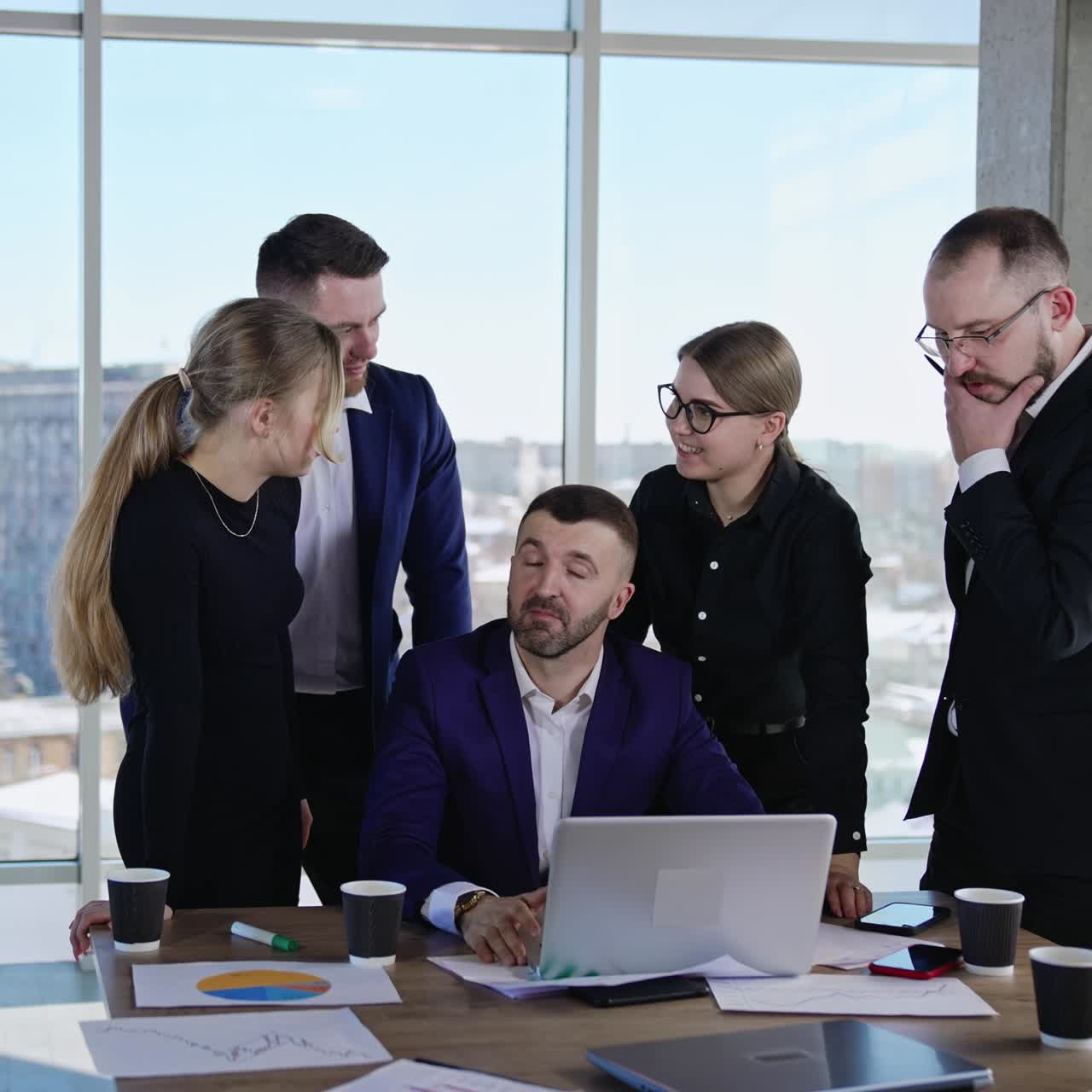 Boss sitting in front of laptop and other coworkers stand beside him. Brainstorming and discussing ideas in the positive and easy working atmosphere. Young collective solving working tasks