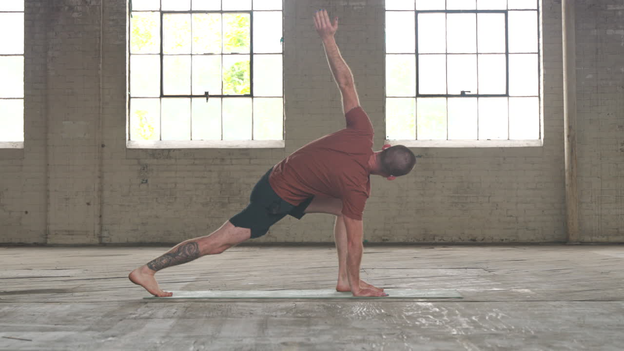Man in an industrial warehouse practicing yoga, the pose of inverted runners lunge.