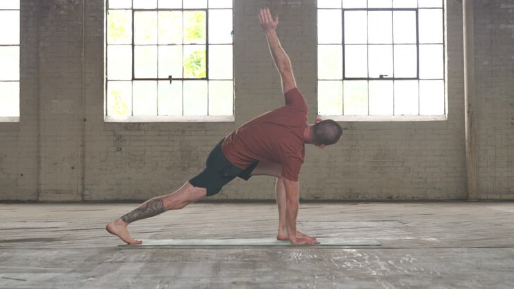 Man in an industrial warehouse practicing yoga, the pose of inverted runners lunge.