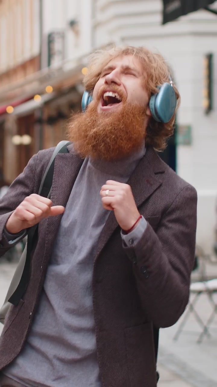 Giovane felice con le cuffie wireless che ascolta la sua musica energetica preferita in una strada della città urbana