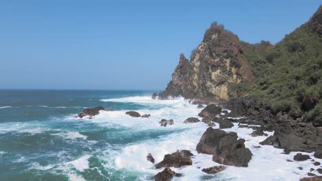 Fliegen-Sie-In-Geringer-Höhe-über-Einen-Felsigen-Strand,-Während-Das-Meerwasser-Von-Den-Wellen-Auf-Den-Felsen-Spritzt