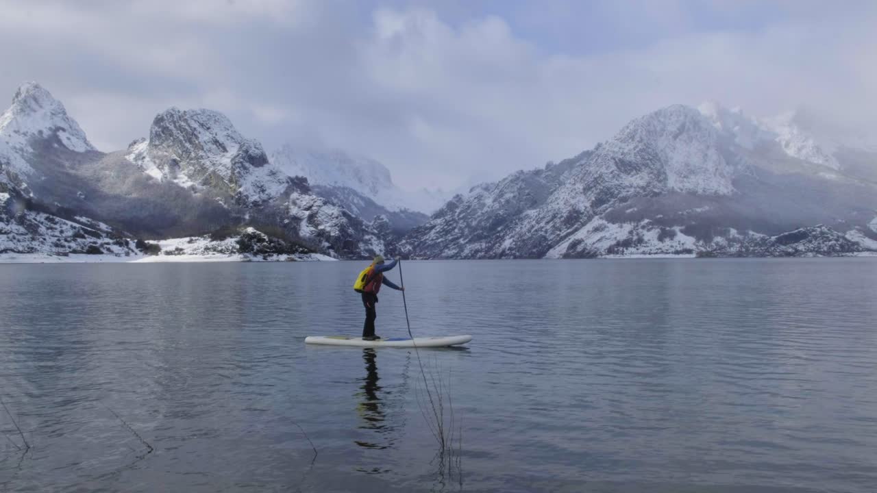 hombre en paddle board entre el agua y las montañas en la costa
