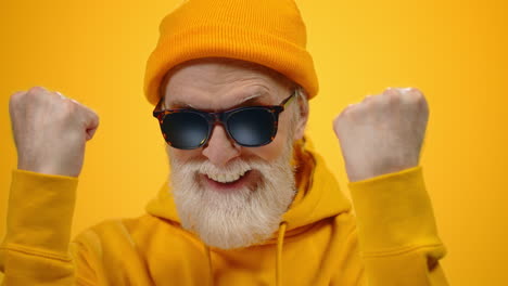 Cheerful-aged-man-enjoying-time-in-studio.-Old-guy-raising-hands-indoors.