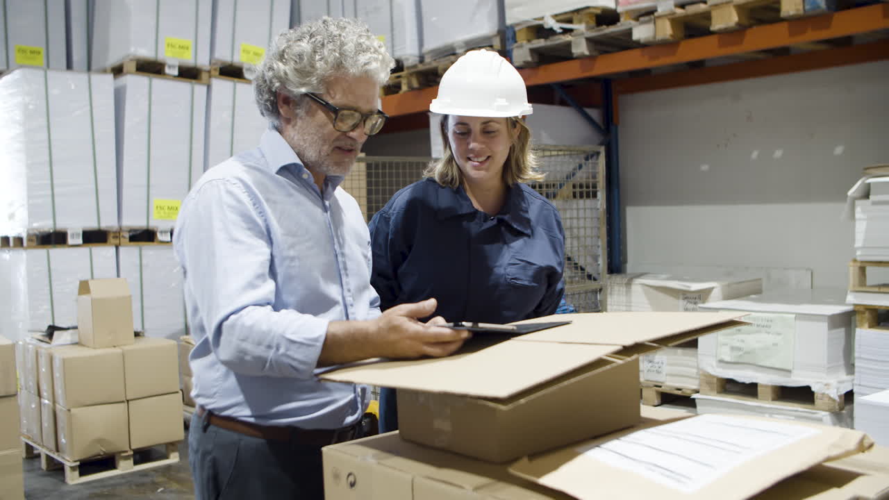 улыбающийся начальник и сотрудница разговаривают на складе, проверяя документы на планшете
