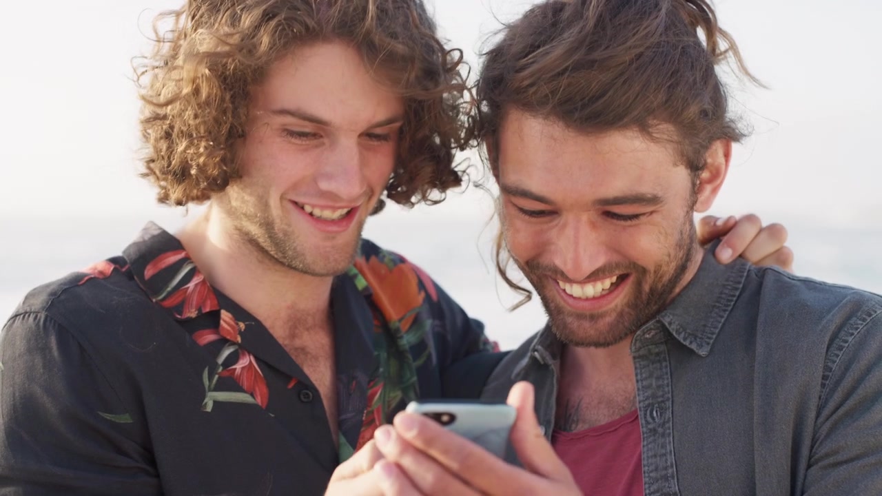 Two Young Men Laughing While Looking at a Smartphone Together
