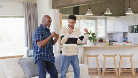 Excited-african-american-father-and-adult-son-cheering-at-sport-on-tv-and-embracing,-slow-motion