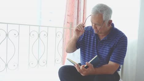 Portrait-of-senior-man-reading-book-relaxed-in-bedroom