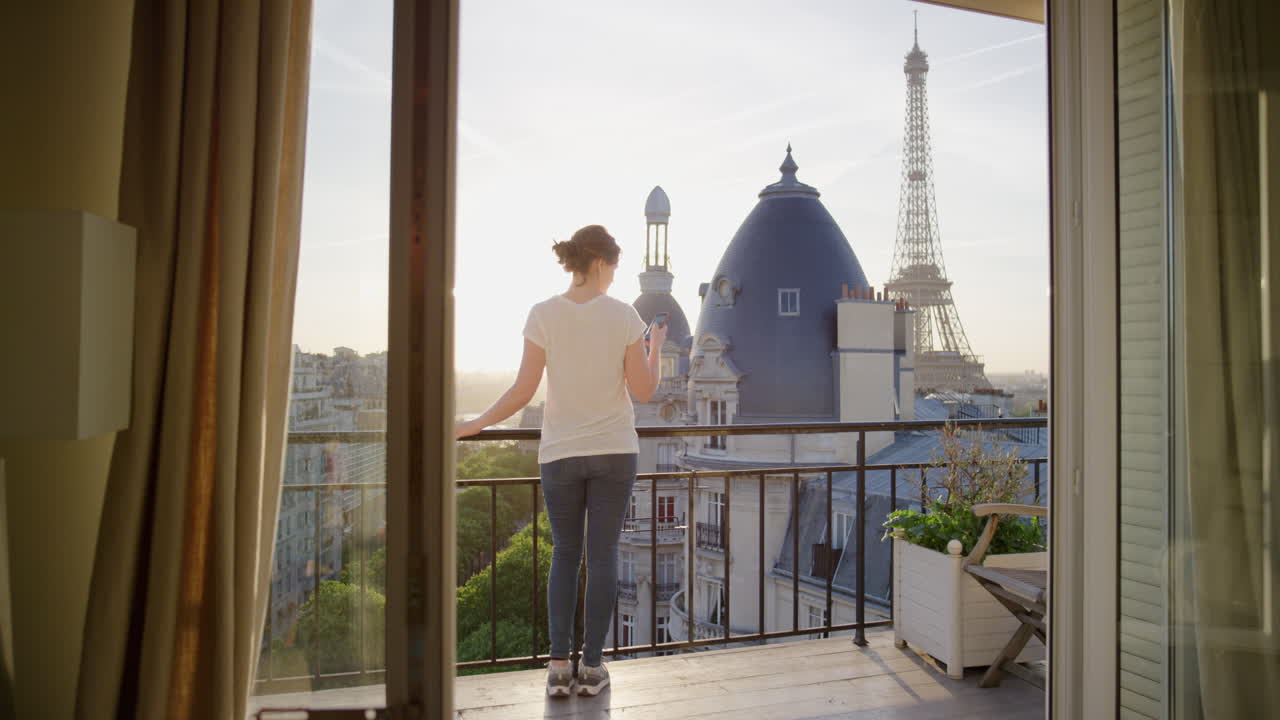 donna felice che usa lo smartphone che scrive messaggi sul balcone a parigi in francia che si gode la vista della torre eiffel che condivide l'esperienza di vacanza che naviga sui social media un bel tramonto