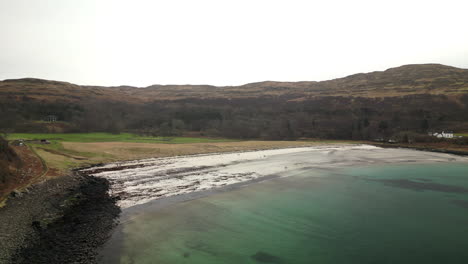 forward pan aerial of water body surrounded by hills and trees by wide beach