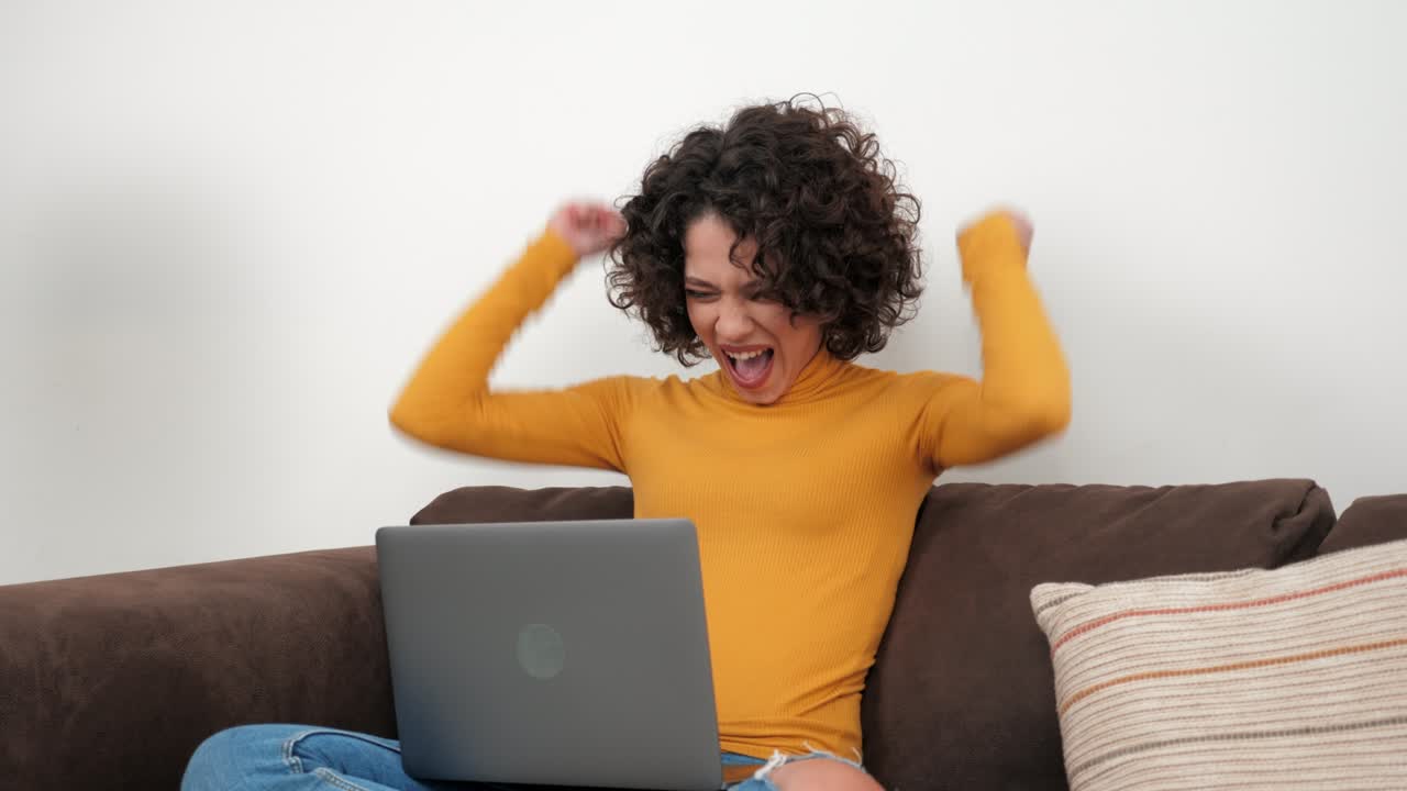 Entusiasta studentessa riccia vincitrice che celebra l'ammissione all'università, con laptop