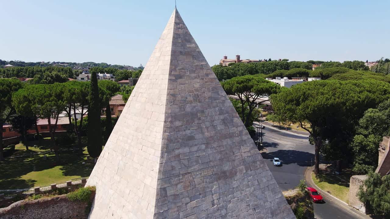 Iconic white stone pyramid monument from ancient Rome by modern street, pine trees