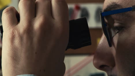 Closeup-shot-of-detective's-profile-as-he-follows-and-records-the-suspect's-actions-with-binoculars-and-a-tape-recorder