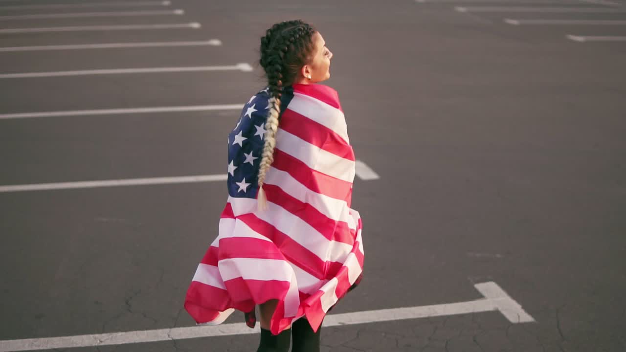 Proud american girl walking and wrapping the american flag over her shoulders looking at the camera. Slow Motion shot