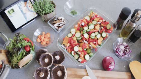 Overhead-view-of-vegetables-in-baking-dish-and-ingredients-on-kitchen-worktop,-slow-motion