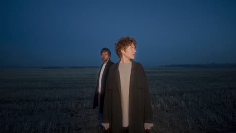 couple standing together in field and looking around in evening