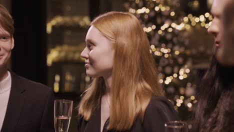 close up view of a red haired girl wearing elegant clothes while talking with her friends and holding a glass of champagne at the new year's party