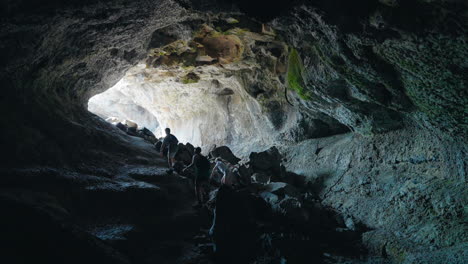 people exploring a large cave towards a bright opening