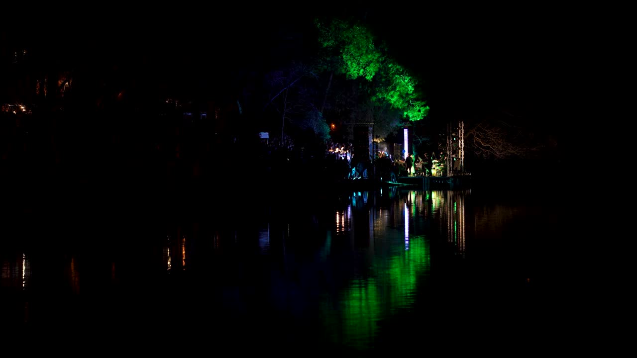luces multicolores en el concierto nocturno en vivo, cantante con grupo de música actuando cerca del lago del parque de la ciudad