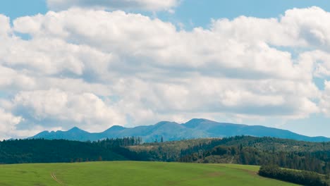 Sich-Schnell-Bewegende-Wolkenzeitraffer-über-Hügeln-Und-Wiesen-Mit-Wald-Und-Bergkette-In-Der-Ferne