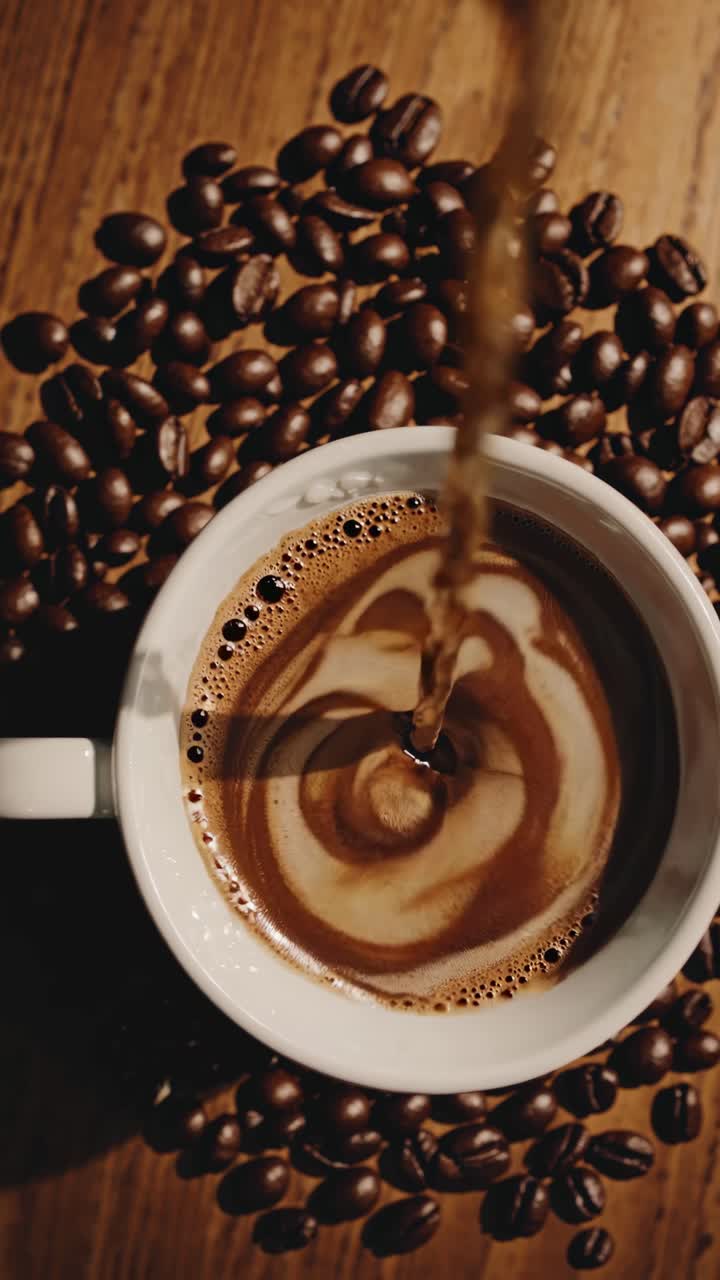 Top-down video af kaffe, der hældes i en kop omgivet af bønner, der fanger hvirvlende mønstre.