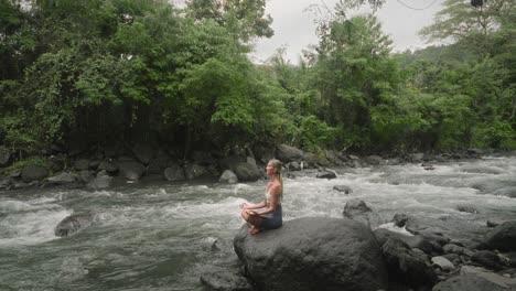 mujer milenaria rubia durante la curación de la naturaleza en sukhasana pose fácil en roca