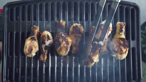 Vista-De-Arriba-Hacia-Abajo-Del-Pollo-Carbonizado-Que-Se-Voltea-Con-Pinzas-En-La-Parrilla-De-La-Barbacoa