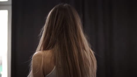 disheveled girl is awake and standing before window, opening curtains and looking through the window