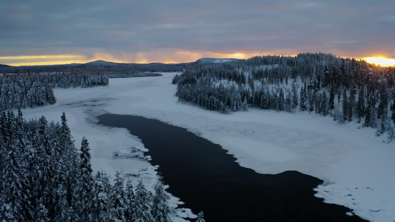 Beautiful aerial view orbiting right across snowy Lapland Sweden winter lake landscape forest trees at sunrise