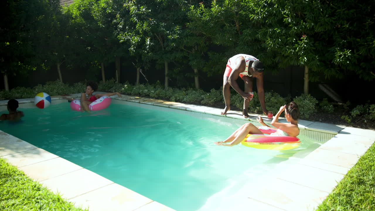 Diverse friends enjoying sunny day by pool, relaxing on floats with drinks in hand