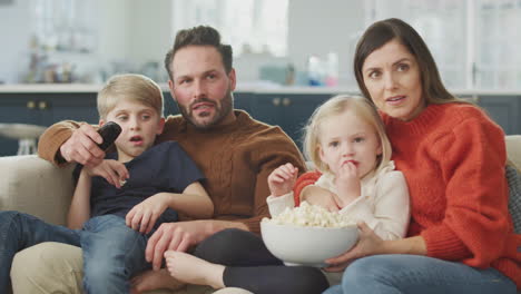 familia sentada en el sofá con palomitas de maíz viendo una película de miedo en la televisión juntos