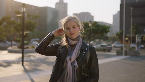 slow motion portrait of cute young blonde woman student running hand through hair smiling happy in windy city wearing leather jacket