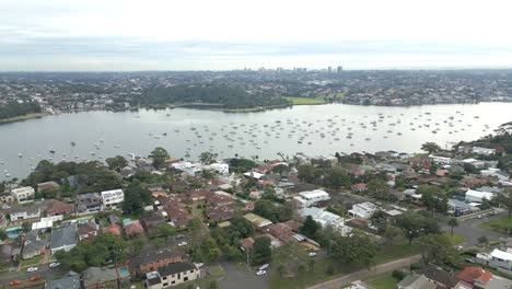 Flying-over-neighborhood-town-with-residential-homes-and-houses-with-boat-marina-in-the-background