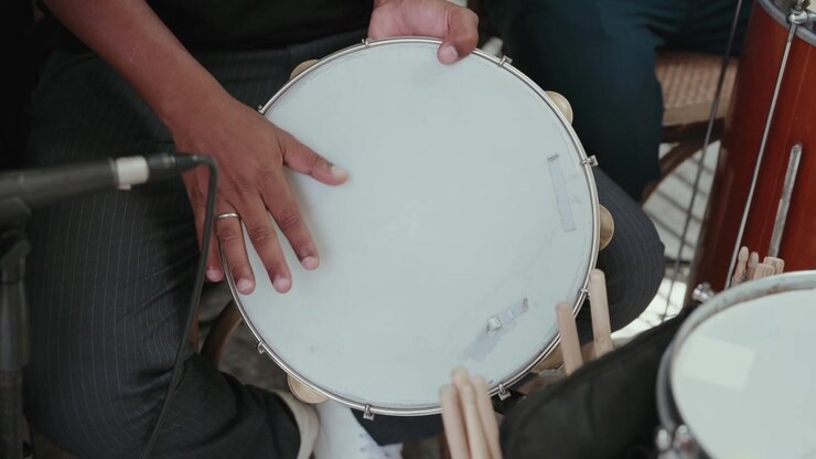 Mani di un musicista che suonano un tamburello, creando ritmo e musica durante un'esibizione dal vivo con altri strumenti