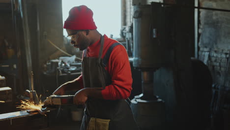 african american blacksmith doing metalwork with angle grinder at workshop