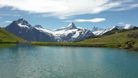 dramatic close over water aerial view of blue mountain lake in the swiss alps with dramatic snow covered mountain peaks backdrop, bachalpsee grindelwald first, switzerland