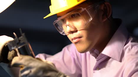 asian young engineer working and using tools measurement quality of metal parts. man wearing hardhat helmet safety with working workshop. concept of engineering, career, industry, manufacture, securit