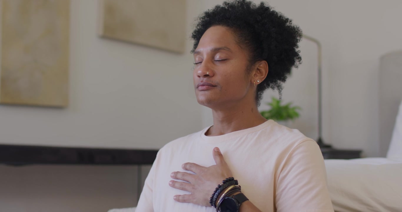 African American adult woman closing eyes calming on sofa placing right hand on chest showing watch